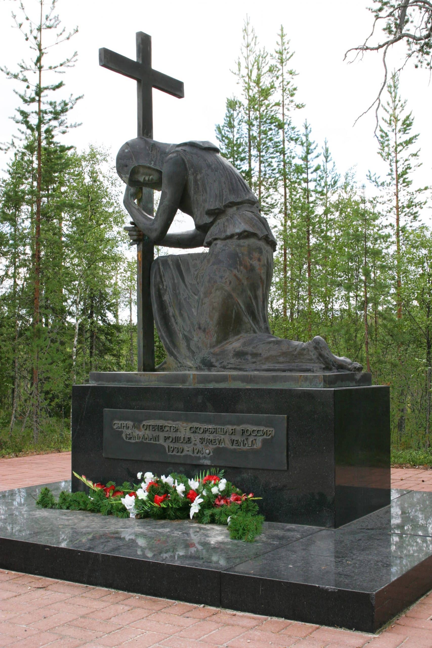 Muistomerkissä isohko risti, johon itkevä nainen nojaa.