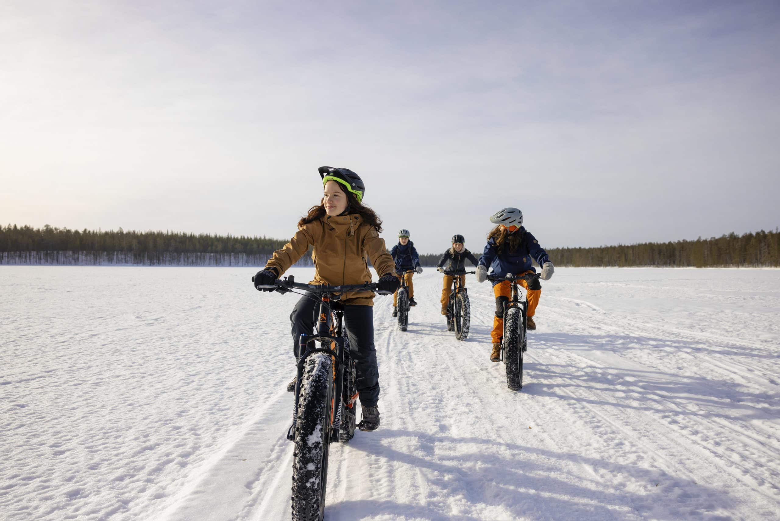 Neljä nuorta aikuista pyöräilee fatbike-paksupyörillä järven jäällä.