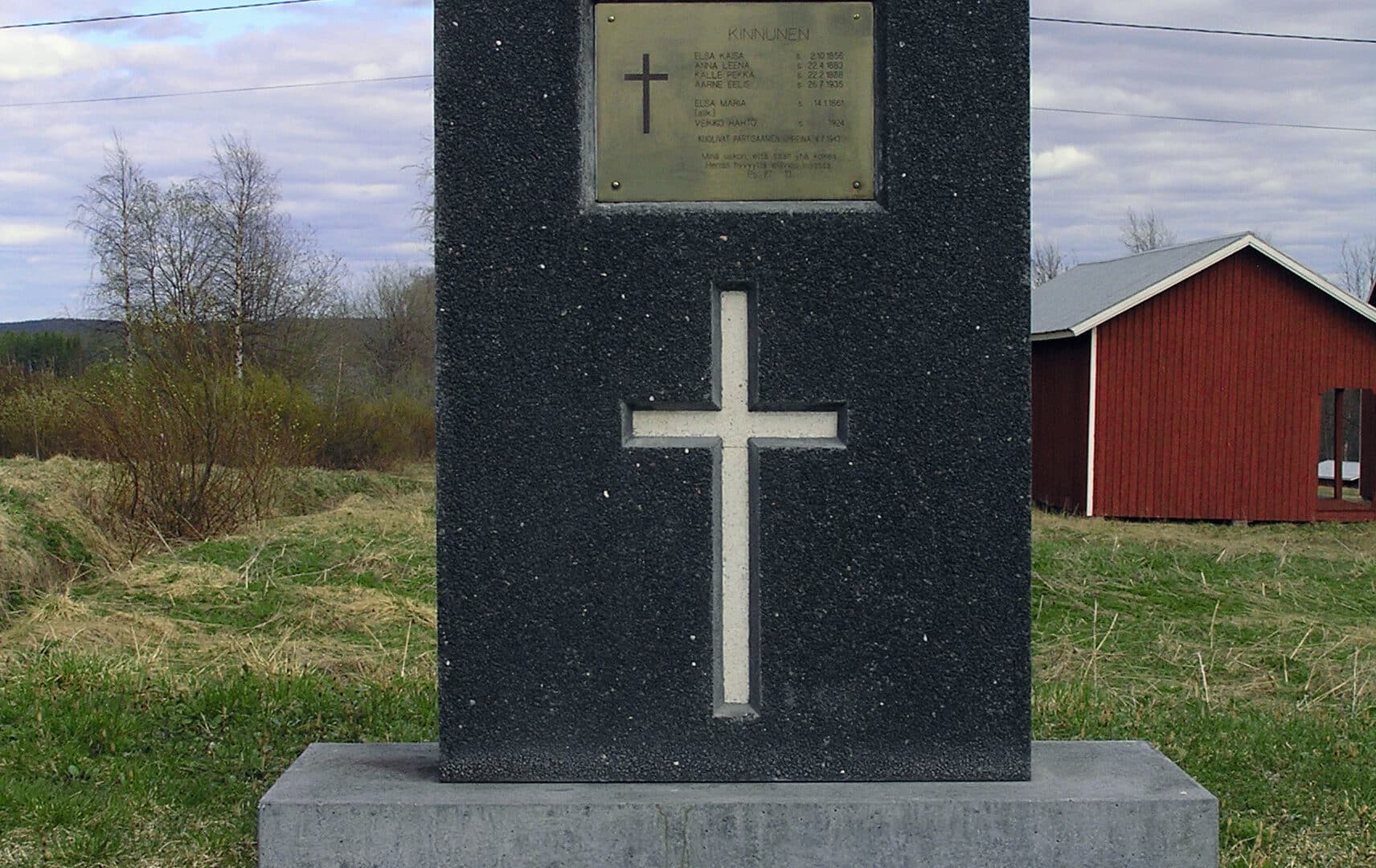 Muistomerkki, jossa ristin kuva ja laatta, jossa lueteltu partisaani-iskussa menehtyneiden nimet.