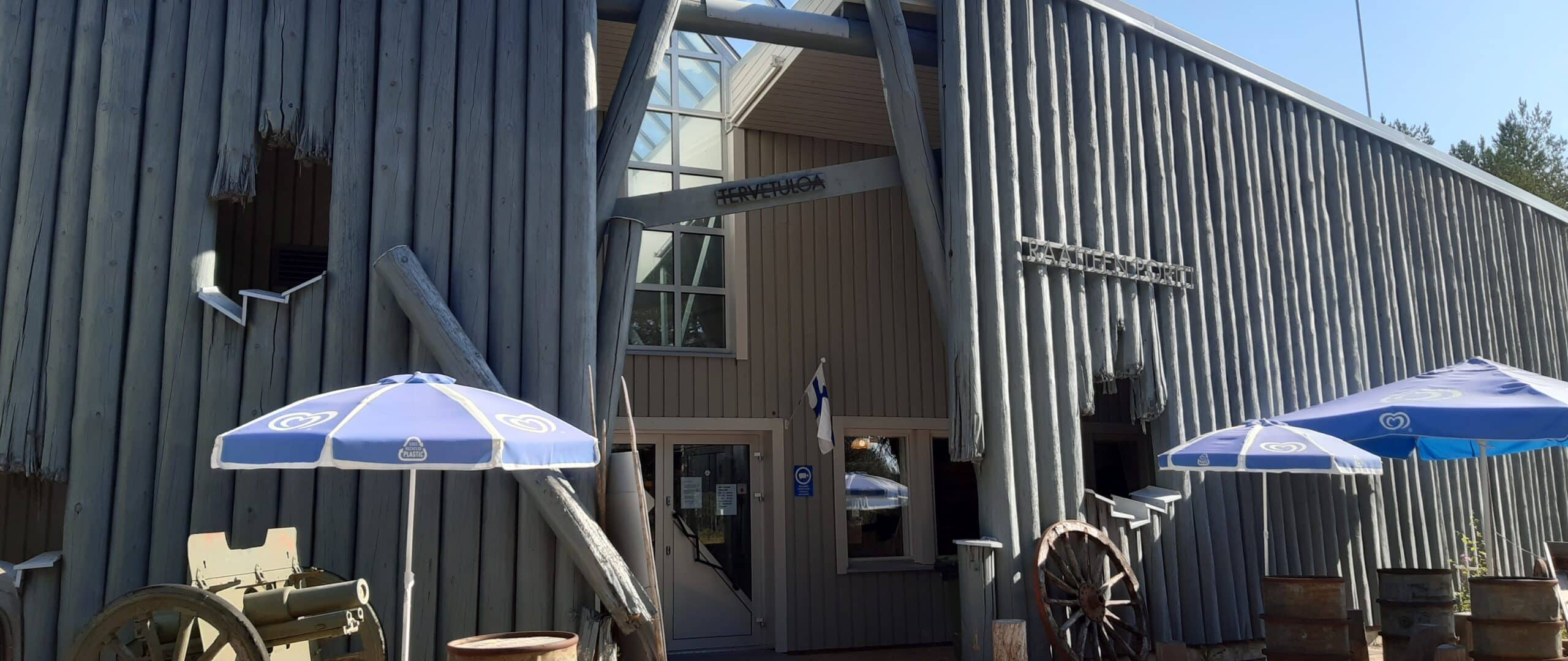 raatteentie päämaja Raatteen Portin sisäänkäynti, jonka molemmin puolin siniset aurinkovarjot.