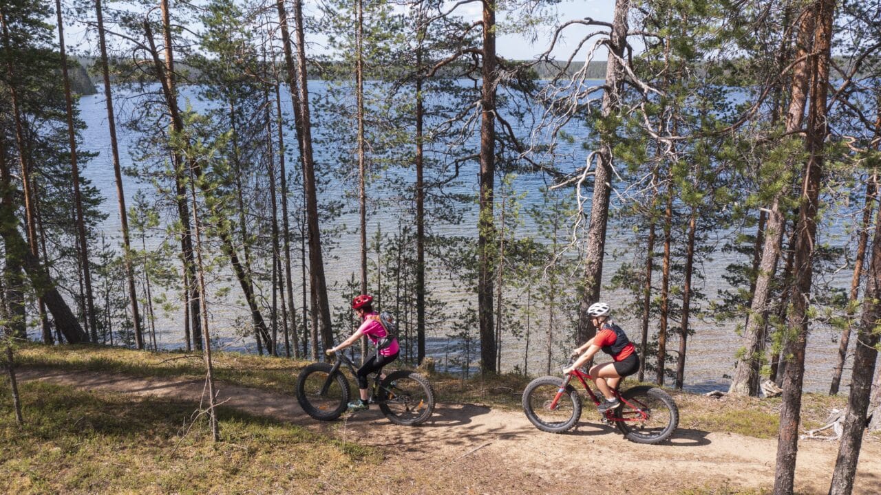 Hossa kansallispuisto Kaksi maastopyöräilijää Iso-Valkeisen rannassa hiekkaharjun päällä kulkevalla maastopyöräreitillä.