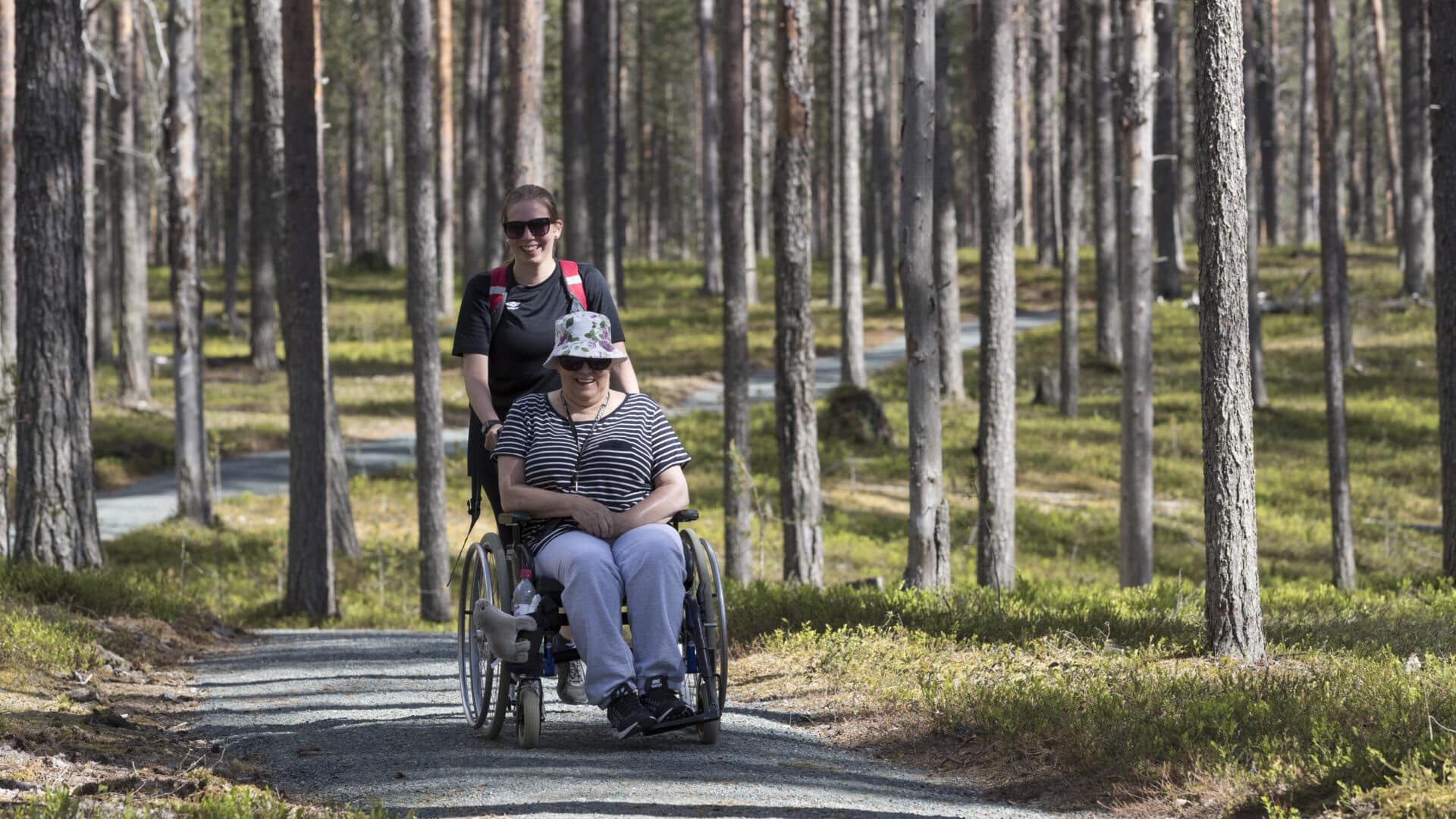 Muikkupuron mutkan esteettömällä retkeilyreitillä nainen pyörätuolissa sekä avustaja.