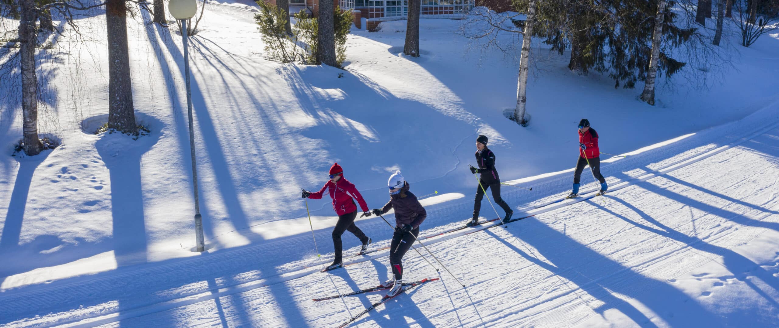 Neljä hiihtäjää Suomussalmen hiihtoladulla Kylpylä Kiannon Kuohujen takana.