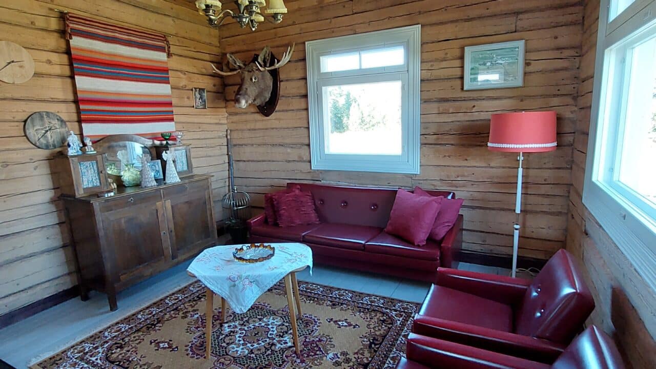 Pirtin alakerran huoneessa on maalattu lankkulattia, punaiset nahkakalusteet ja puinen senkki.