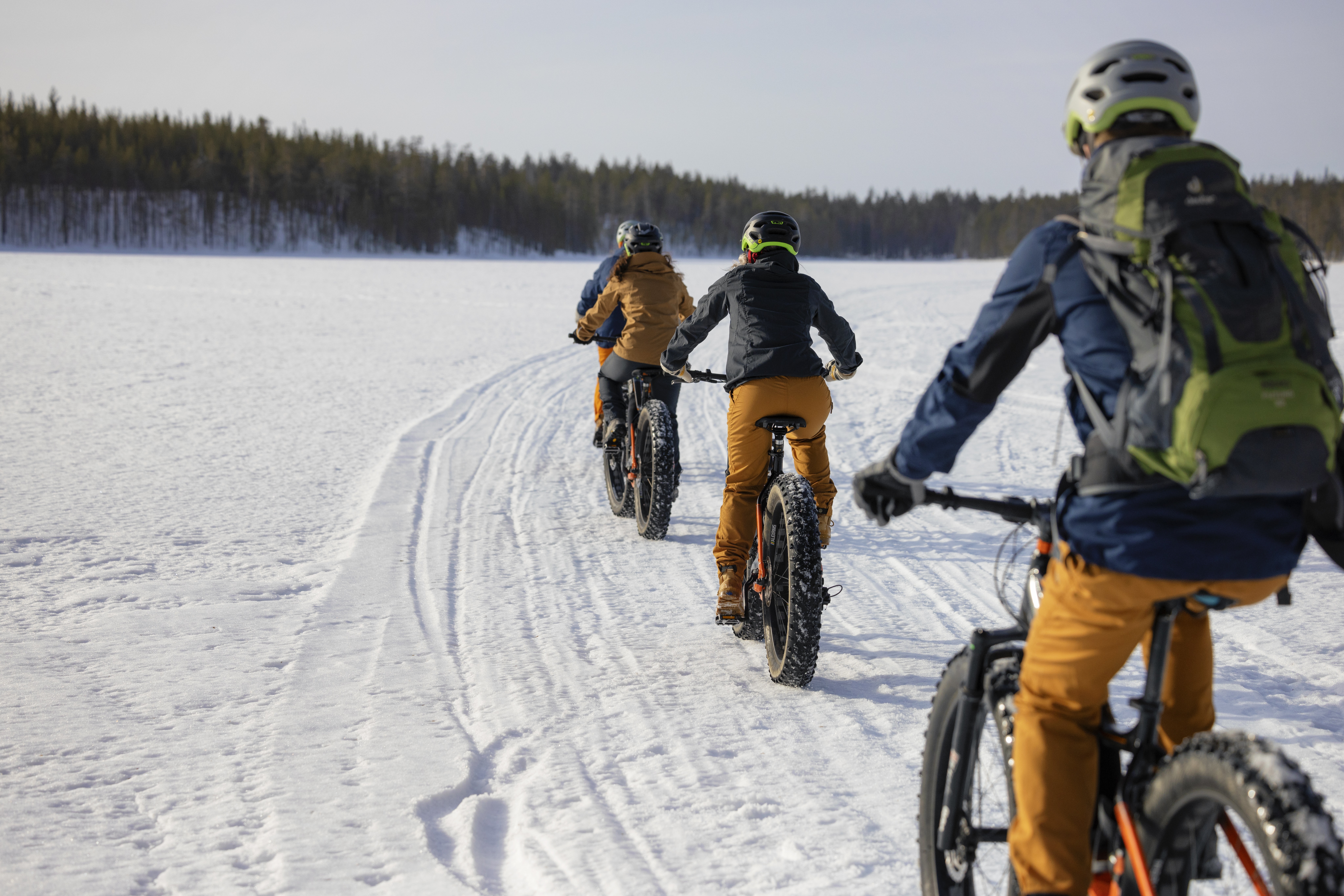 Joukko pyöräilee järvenjäällä auringoisessa talvimaisemassa.