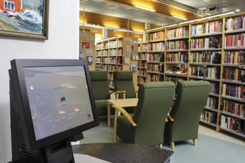 Suomussalmen kirjaston sohvat, kirjahyllyt sekä tietokone.