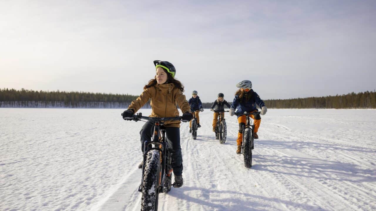 Neljä henkilöä talvipyöräilemässä Hossassa järven jäällä kevätauringossa.
