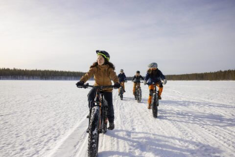 Neljä henkilöä talvipyöräilemässä Hossassa järven jäällä kevätauringossa.