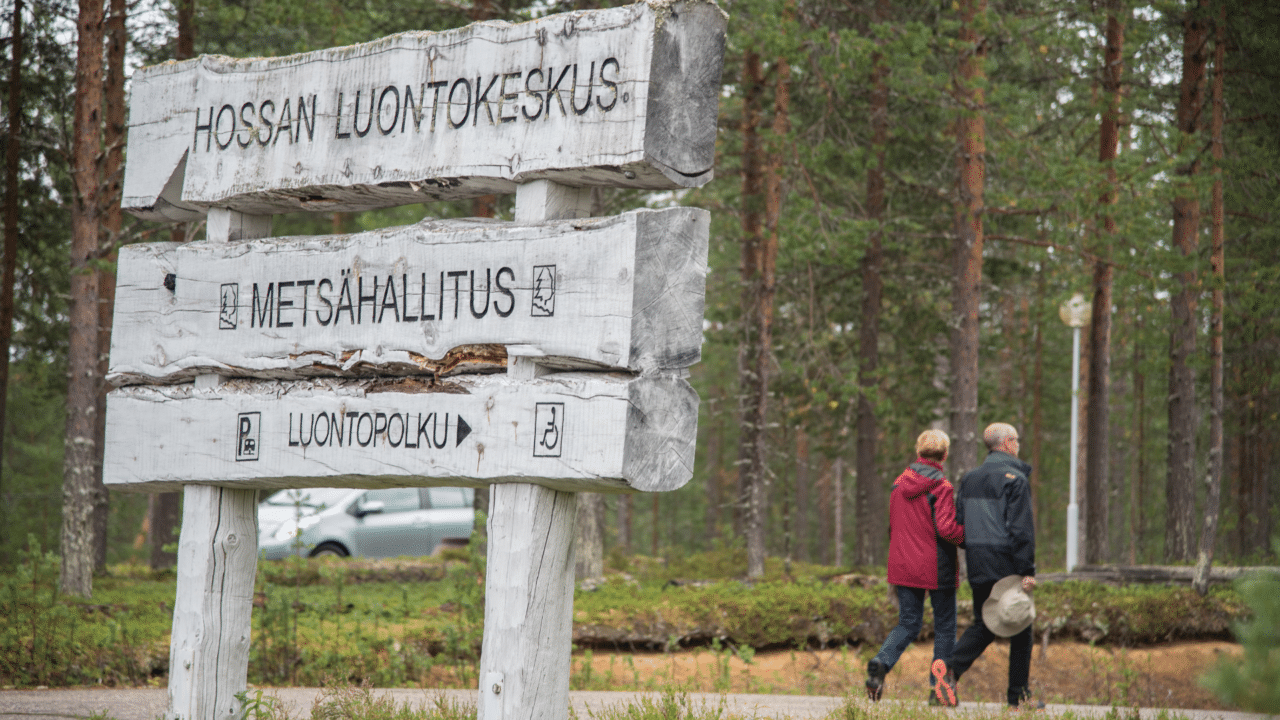 Hossan luontokeskuksen opastekyltit ja kaksi kävelijää.