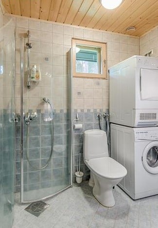 Mökki Villa Lähteenkorvan kylpyhuone jossa suihkukaappi WC-istuin ja pyykinpesukone ja kuivausrumpu