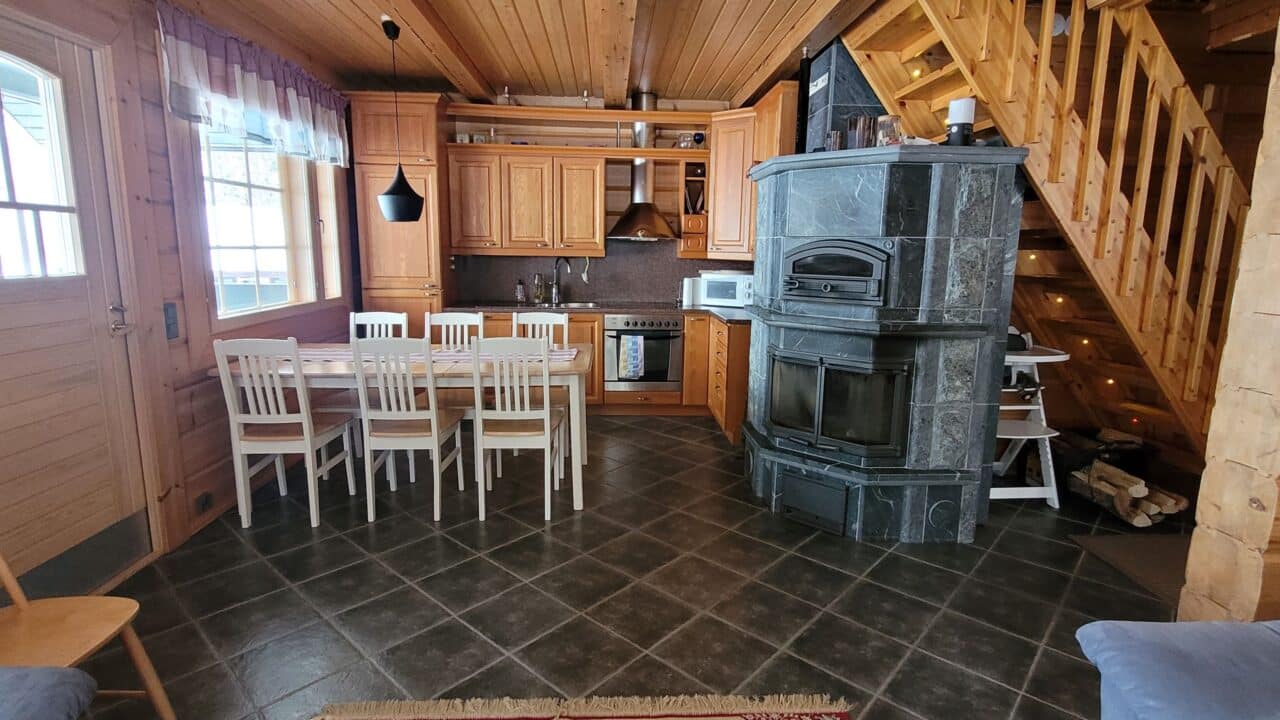 Keittiössä vuolukivinen takka-leivinuuni, kivilattia ja valkoinen ruokapöytä kuudelle hengelle.