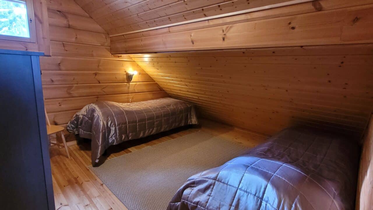 Yläkerran makuuhuoneessa kaksi erillistä vuodetta, joissa molemmissa ruskeat sängynpeitot.