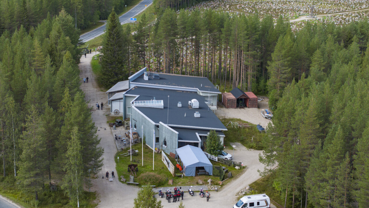 Ilmakuva Raatteenportin talvisotamuseosta. Kuvassa näkyy Talvisotamuseo sekä sen ympäröivää metsää. Lisäksi kuvassa ihmisiä ja henkilöautoja museon parkkipaikalla.