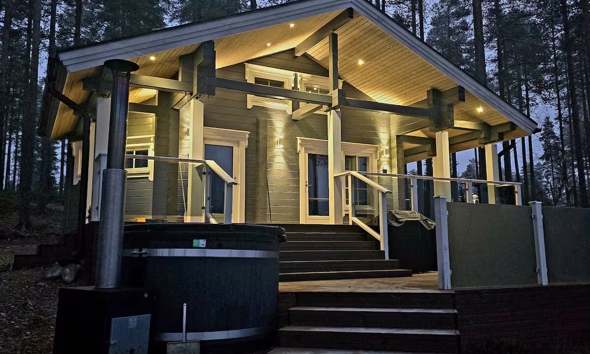 Valaistu mökin kuisti jonka yhteydessä terassi ja palju.