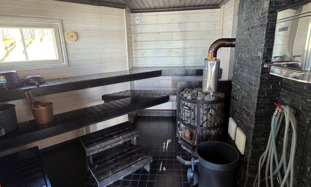 Mustassa saunassa iso kiuas ja valkoinen WC-istuin.