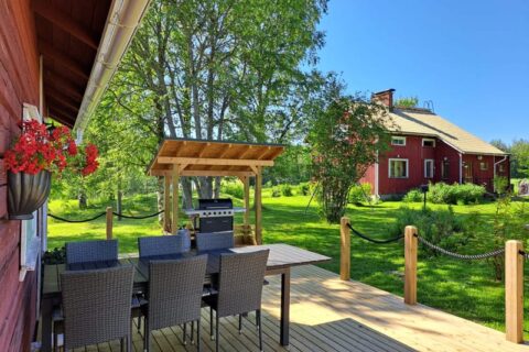 Punainen talo ja ulkosaunan terassi, missä puutarhakalusteet ja erillinen grillikatos.