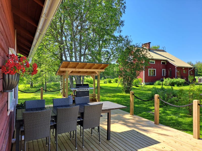 Punainen talo ja ulkosaunan terassi, missä puutarhakalusteet ja erillinen grillikatos.