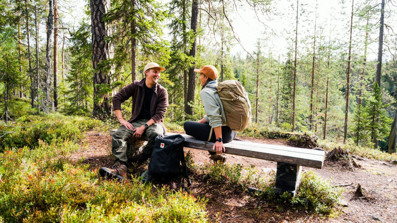Kaksi retkeilijää istuu retkeilyreitin vieressä olevalla penkillä Hossassa.