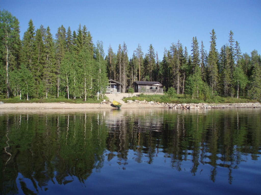 Järven rannalla, metsän ympäröivänä harmaa mökki ja saunatupa