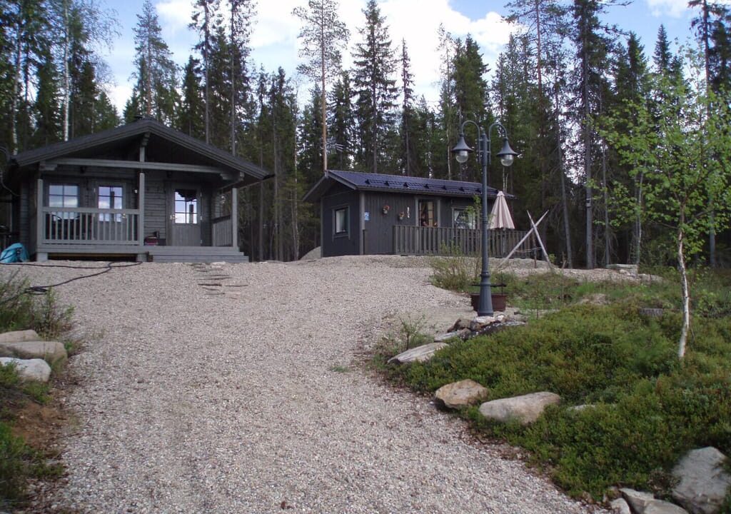 Kellokanervan harmaa mökki ja saunatupa hiekka-/nurmikkomaastossa